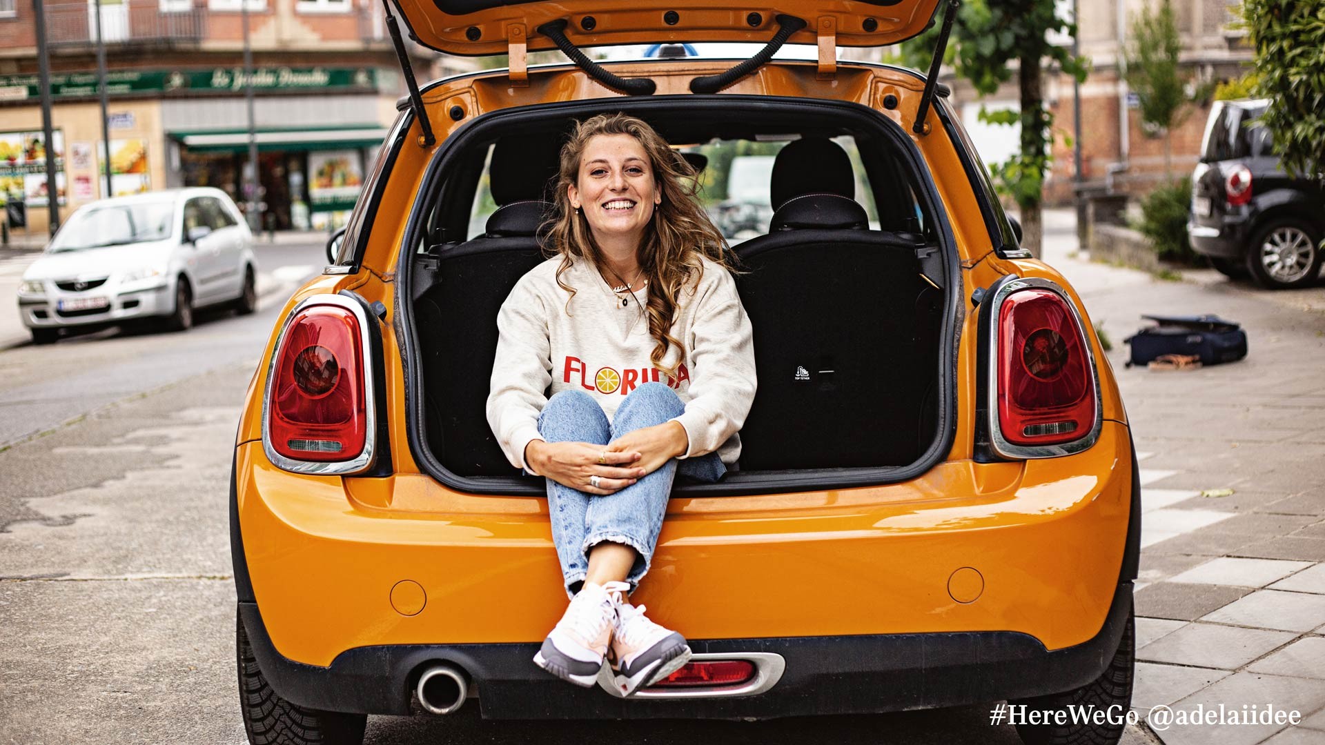 MINI 3-door hatch in volcanic orange with happy woman sitting in trunk